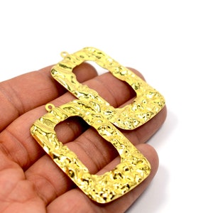 May include: Two gold-toned metal rectangular earring blanks with a textured surface and a hole at the top for attaching earring hooks.