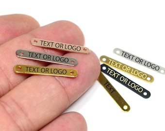 May include: Five metal tags with holes for attaching to items. The tags are in different colors: gold, silver, rose gold, black, and a lighter shade of gold. Each tag has the text "TEXT OR LOGO" engraved on it.