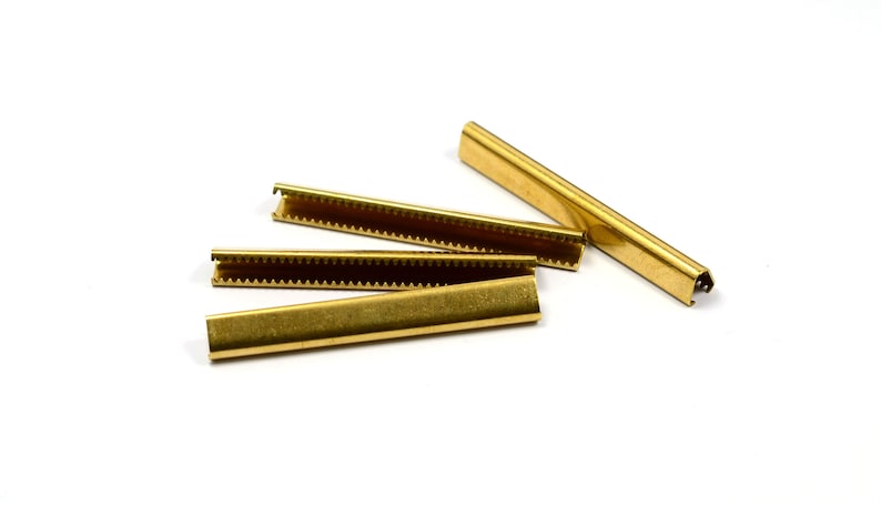 Puede incluir: Cuatro tiras de metal de color dorado con un borde dentado. Las tiras se utilizan para asegurar tela u otros materiales.