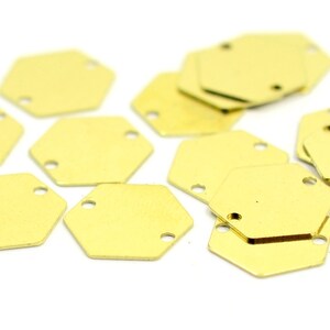 May include: A group of 10 gold-colored metal hexagon-shaped charms with two holes in each charm. The charms are scattered on a white surface.