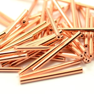 May include: A pile of rose gold colored metal tubes. The tubes are about 1 inch long and have a smooth, shiny finish.