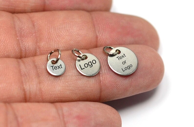May include: Three silver metal round charms with jump rings. The charms are different sizes. The smallest charm says "Text". The middle charm says "Logo". The largest charm says "Text or Logo".