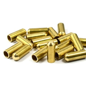 May include: A pile of brass caps, some with a rounded top and some with a flat top. The caps are all the same size and are arranged in a random pattern.