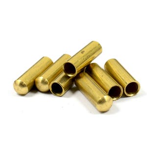 May include: A group of six brass electrical terminal ends. The ends are cylindrical with a rounded top and a hole in the center. The ends are arranged in a pile.