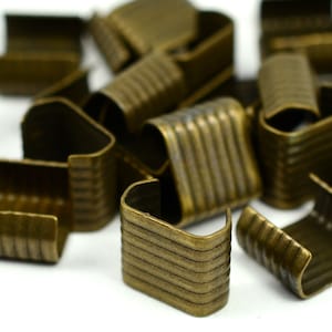 May include: A pile of antique gold metal slider buckles. The buckles have a ridged design and are used for attaching straps or belts.