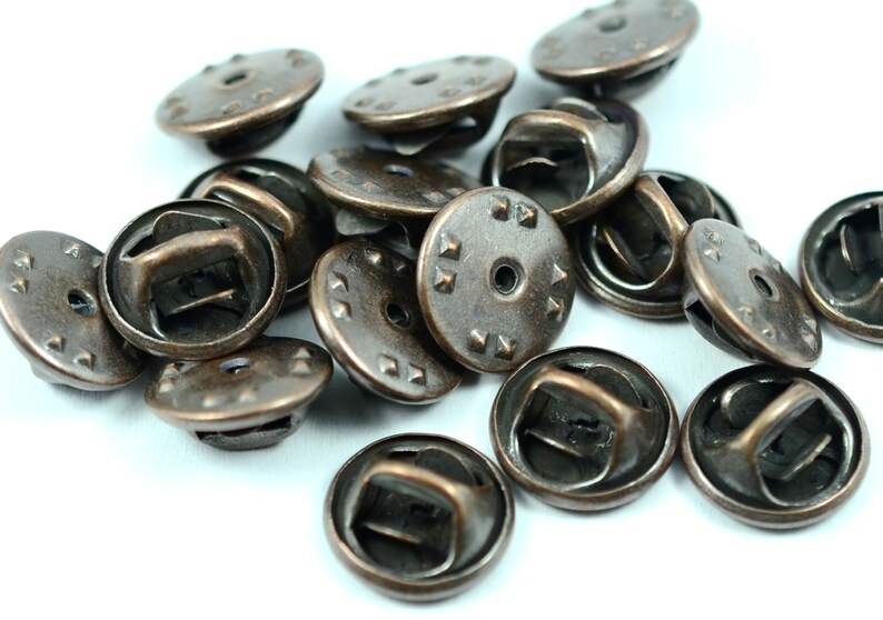 Puede incluir: Un mont&oacute;n de 15 botones de cierre de metal de color bronce antiguo con un dise&ntilde;o decorativo. Los botones tienen una parte superior redonda con un peque&ntilde;o agujero en el centro y un bucle en la parte posterior.