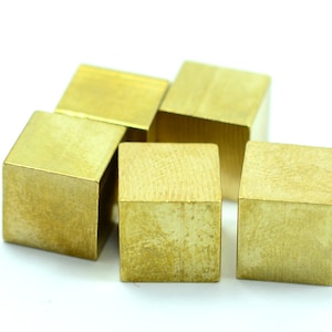 May include: Five small, gold-colored metal cubes arranged in a pyramid shape on a white background.