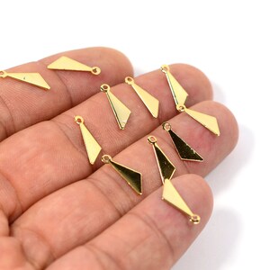 Puede incluir: Una colección de dijes triangulares de metal dorado con un bucle en la parte superior. Los dijes están dispuestos en una mano.
