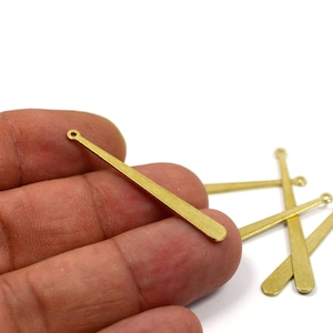 May include: A close-up of five gold-coloured metal earring findings. The findings are shaped like small, flat bats with a small hole at the top.