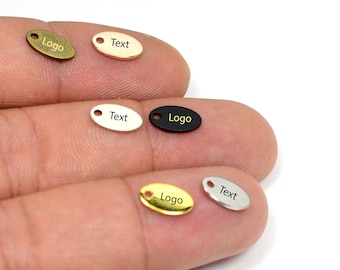 May include: Five oval-shaped metal tags with jump rings. The tags are in different colors: gold, silver, black, white, and bronze. The tags are engraved with the words "Logo" and "Text".