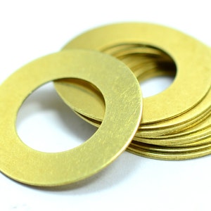 May include: A stack of brass washers, with one washer laying on its side. The washers are a shiny gold color and have a smooth, slightly textured surface.