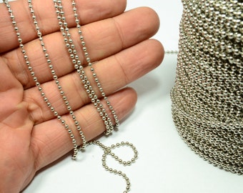 May include: A silver ball chain with multiple strands, shown on a hand and coiled up. The chain is made of small, round metal beads.