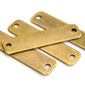 Può includere: Quattro etichette rettangolari in metallo color oro antico con due fori ciascuna. Le etichette sono impilate l'una sull'altra.