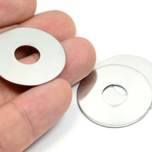 May include: Three silver metal washers, one in a hand and two stacked together on a white surface.