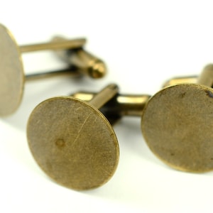 May include: Close-up of three antique brass cufflinks with a circular design. The cufflinks have a classic, vintage aesthetic, with a warm, metallic finish. The design is simple and elegant, suitable for formal wear.