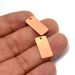 May include: Two small, rectangular copper tags with a hole at the top. The tags are a warm, reddish-brown color.