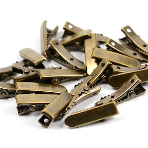 May include: A pile of antique gold metal hair clips. The clips are all the same size and shape, and they are arranged in a random pattern.
