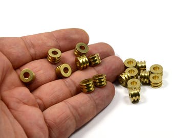 May include: A hand holding a group of gold-colored metal beads. The beads are round with a raised, textured design. There are 15 beads in total.