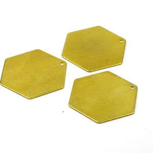 Könnte beinhalten: Drei goldfarbene sechseckige Metallanhänger mit einem kleinen Loch oben.
