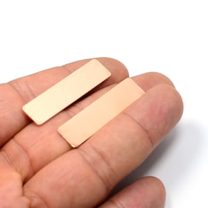 May include: Two rectangular pieces of copper, both are a light copper color, and are laying on a hand.