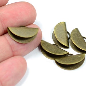 May include: A group of five antique brass half-circle metal clasps with a small hole at the top. The clasps are stacked on top of each other.