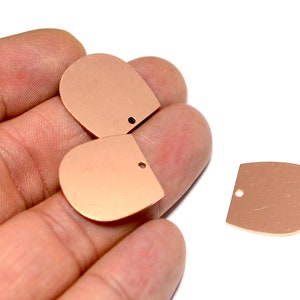 Puede incluir: Tres abalorios de metal de color oro rosa en forma de semicírculo con un agujero en la parte superior. Los abalorios están en una mano.