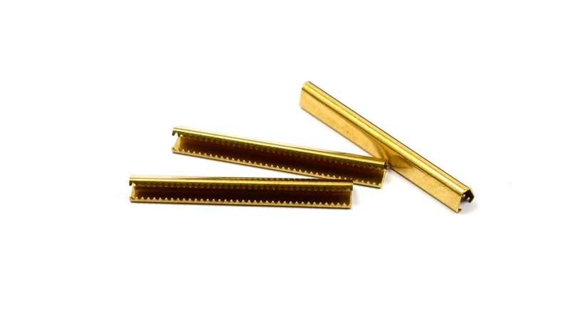 Puede incluir: Tres tiras de metal dorado con un borde dentado. Las tiras se utilizan para sujetar tela a un marco.