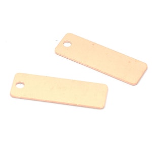 May include: Two small, rectangular, rose gold-colored metal tags with a hole at the top for hanging.