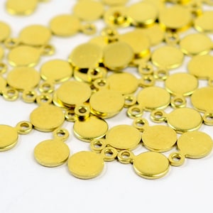 May include: A pile of gold-coloured metal circle charms with a loop on each side. The charms are approximately 2.5 cm in diameter.