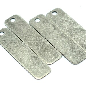 May include: Four silver-toned metal tags with a hole at the top. The tags are rectangular and have a distressed, textured finish.