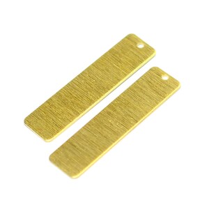 May include: Two gold-colored metal rectangular tags with a hole at the top. The tags have a brushed finish.