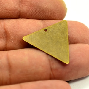 May include: A brass triangle pendant with a hole at the top for hanging. The pendant has a brushed finish and is a light gold color.