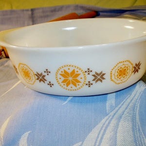 May include: White oval baking dish with a brown and yellow floral pattern. The dish has a scalloped edge and is made of ceramic.