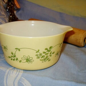 May include: A yellow mixing bowl with a green floral design. The bowl has a white interior and a slightly rounded shape.