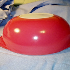 Puede incluir: Un cuenco rojo brillante con interior blanco. El cuenco tiene forma redondeada y borde acampanado. El cuenco es probablemente de vidrio o cerámica y está diseñado para la preparación de alimentos.