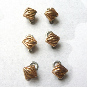May include: A set of six small, square-shaped buttons with a metallic bronze finish. Each button features a raised, geometric, sunburst-like pattern radiating from the center and includes a silver-toned metal loop shank on the back for attachment.