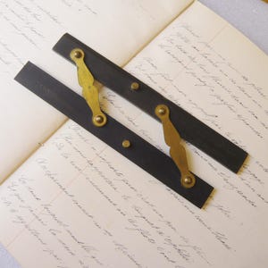 May include: A vintage folding ruler made of two dark wood segments connected by decorative brass hinges and rivets. The wood features a stamped number 1050 on one end. The tool is constructed with a pivot mechanism that allows the two straight arms to fold.