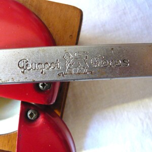 May include: A vintage Peugeot Freres coffee mill featuring a bright red metal top and a wooden base. A horizontal silver metal handle is engraved with the text Peugeot Freres and a lion logo. The mechanism includes visible screws.