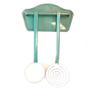 Peut inclure: Un porte-ustensiles de cuisine turquoise vintage avec deux ustensiles assortis. Le support a un dessus incurvé et deux supports verticaux. Un ustensile est une louche pleine, l'autre est une cuillère à fentes.
