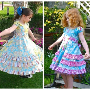 May include: Two young girls wearing colourful floral dresses with multiple layers of ruffles. The dresses have a blue base with pink and yellow accents. The girls are standing in a garden setting.