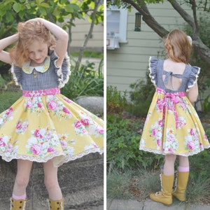 May include: A young girl wearing a yellow and pink floral dress with a gray and white striped bodice and a white collar. The dress has a lace trim and a pink ribbon tied at the waist. The girl is wearing yellow boots.