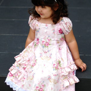 May include: A young girl wearing a white headband with a floral print dress and white lace trim. She is wearing sparkly gold shoes and is sitting on a step.