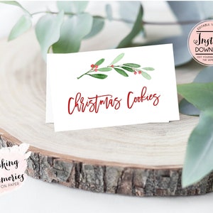May include: White card with the words "Christmas Cookies" in red script, adorned with a watercolor sprig of green leaves and red berries. The card is on a wooden slice, with text that says "Making Memories on Paper".