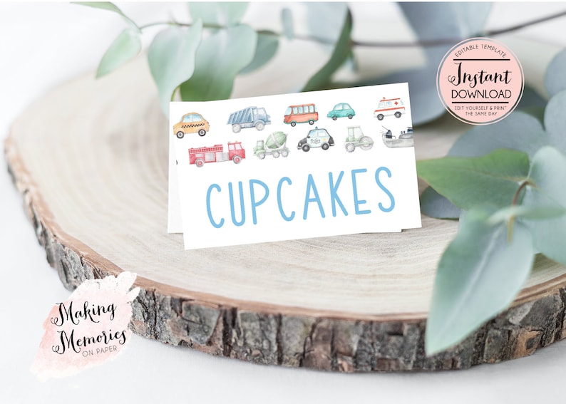 Op de afbeelding: Een witte kaart met het woord "CUPCAKES" in lichtblauw, met aquarel illustraties van diverse voertuigen. De kaart ligt op een houten schijf, met de tekst "Making Memories ON PAPER".