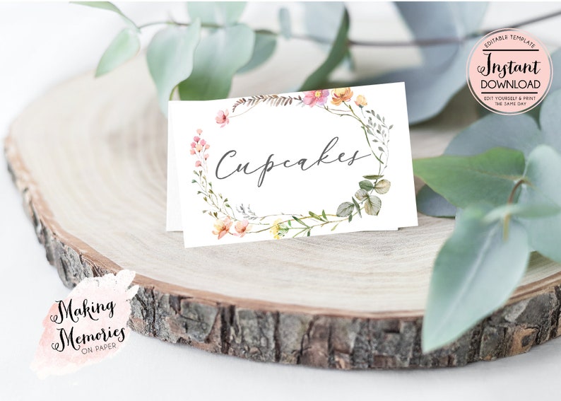 K&ouml;nnte beinhalten: Druckbarer Schild mit einem floralen Kranzdesign und dem Text "Cupcakes". Das Schild befindet sich auf einer Holzscheibe mit gr&uuml;nen Bl&auml;ttern.