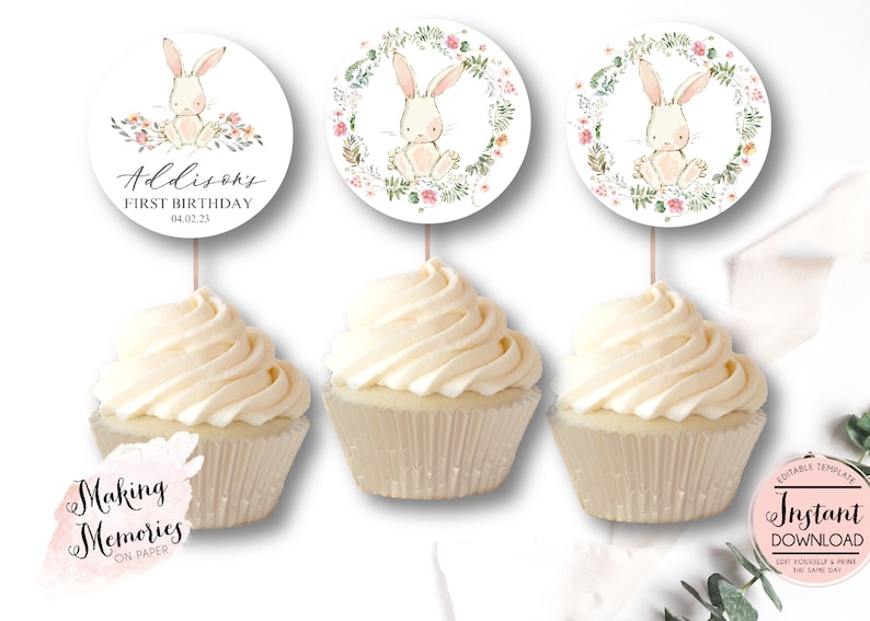 May include: Three cupcake toppers featuring a watercolor illustration of a bunny rabbit in a floral wreath. The toppers are printed on white cardstock and have a pink and green color scheme. The text on the topper reads "Addison's First Birthday 04.02.23".