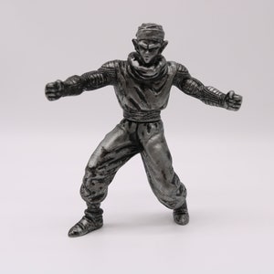 May include: A silver-colored figurine of a character with pointed ears, wearing a turban and a martial arts uniform. The figure is in a dynamic pose with arms outstretched, ready for action. The figure is approximately 6 inches tall.