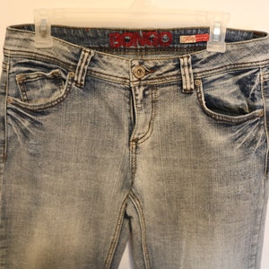 May include: A pair of light blue denim jeans with a faded look. The jeans have a red embroidered "Bongo" logo on the back waistband.