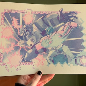 Puede incluir: Ilustración de dos robots en combate, en tonos azules, rosas y grises. Un robot grita, mientras que el otro golpea. La obra está enmarcada por una cadena y un emblema geométrico.