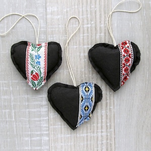 May include: Three black felt heart-shaped ornaments with white and colored embroidery. The ornaments have strings for hanging.